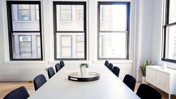 A long conference table with three empty chairs, water glasses, and a small recording device near one place setting